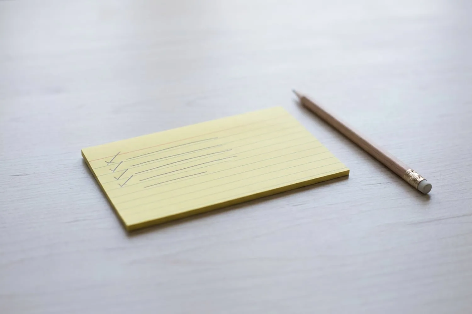 A yellow index card on a pale table with five short pencil lines, the first four ticked off, and a pencil beside it